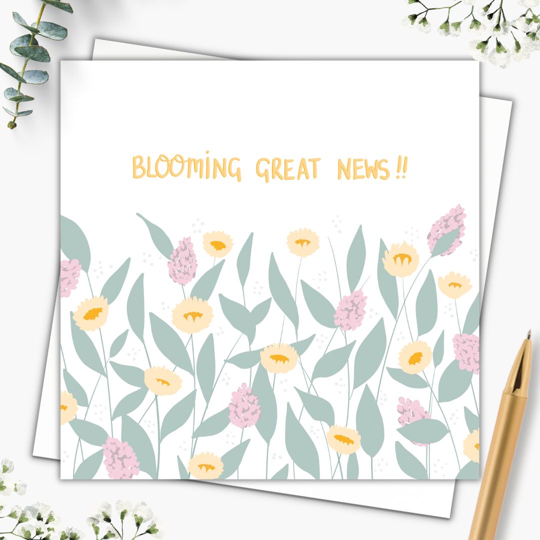 A beautiful botanical celebration card with the words "Blooming great news!!" on the front. The words are hand-written in a yellow gold in the top part of the card. Below it are big green leaves, yellow/orange flowers and large pink and purple flower blossoms. It's pretty, floral and cheerful to look at. It's set on top of a plain white envelope and beside it there is a gold pen.