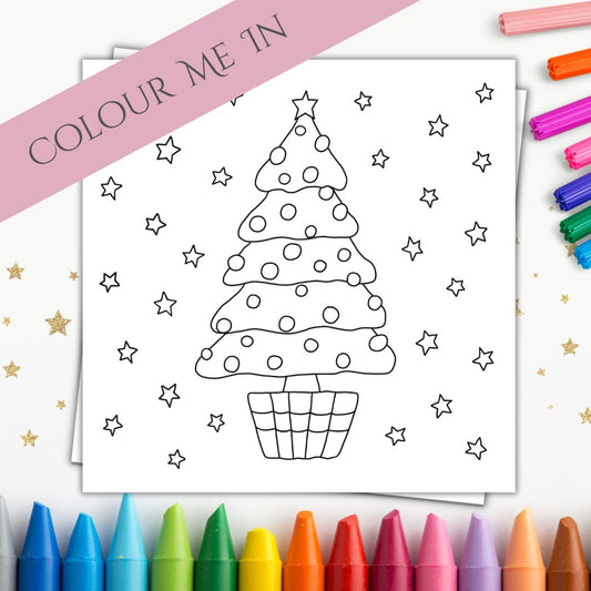 Image shows a Christmas card that is made for coloring in. The front of it is a simple and playful design of a Christmas tree with lots of stars around it. These are all designed to be colored in and there is space to do so. There is an envelope with the card which is tucked in behind it. Surrounding the card are a mixture of markers and crayons to give some colour to the picture and show the purpose of the card. On the top right corner of the image there is a banner which says "Colour Me In".