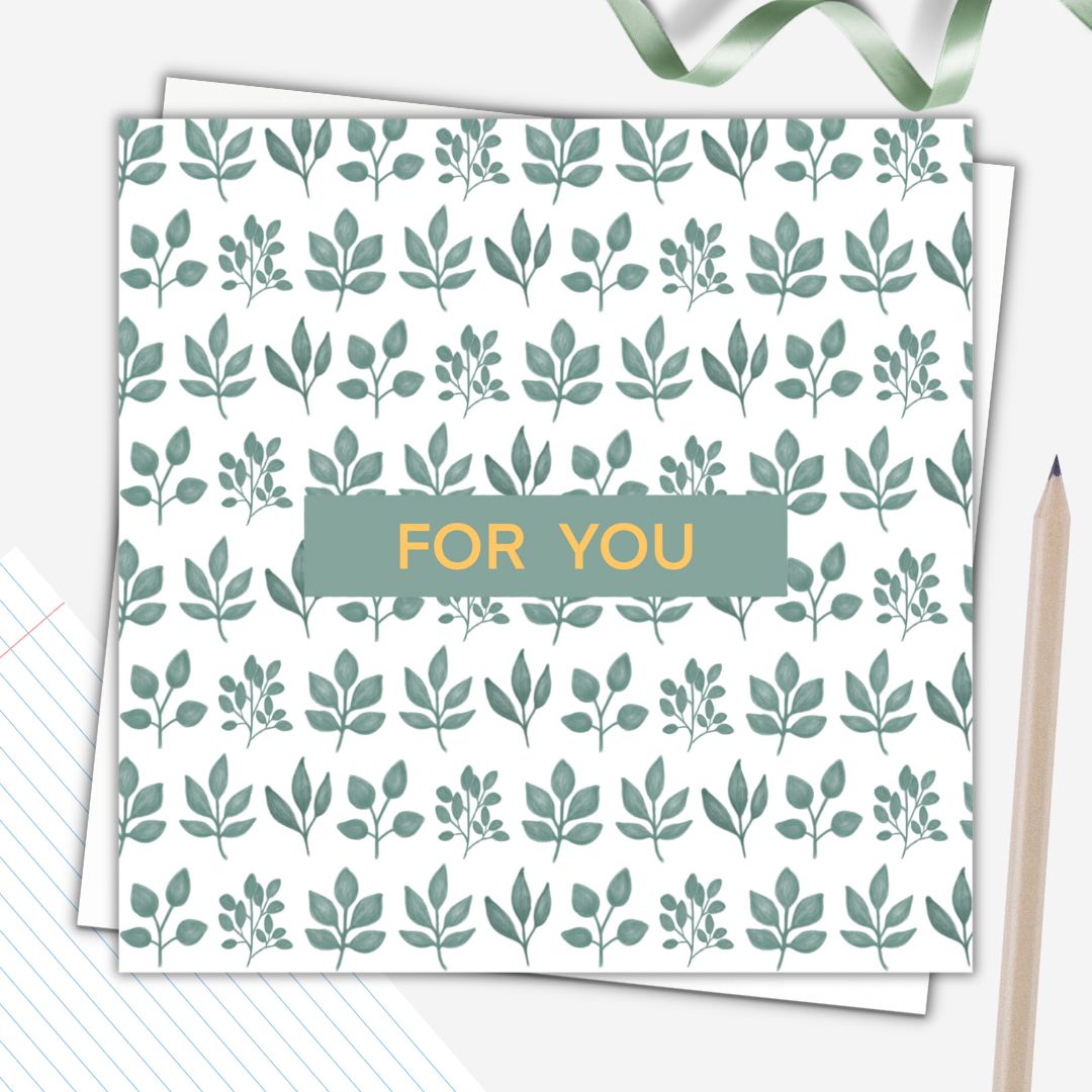 This is a patterned botanical themed greeting card for all occasions. It has the words "For You" in a simple gold font in the centre of the card on a small dark green background. Behind that, the rest of the card is a pattern on clusters of green hand drawn leaves on a white background. The botanical card is set on a plain white envelope and beside it there is a simple pencil
