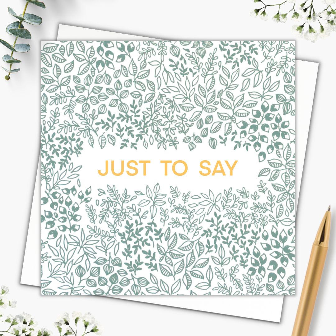 This botanical greeting card says "Just to say" in a gold font in the centre of the card. Surrounding it, the rest of the card is made up of green leafy patterns using different shapes sizes and types of leaves. The sage green colour gives a lovely natural tone to the card and makes it neutral too along with the gold writing. The card is set on top of a plain white envelope and there is a gold pen right beside it.