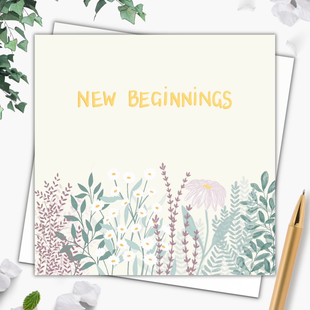 This botanical greeting card has the words "New Beginnings" hand written in gold in the top part of the card. Below it there are clusters of leaves in various shades of green as well as wild flowers, and daisies. The background of the card is a very very faint lemon colour. The flowers and leaves underneath are like a wildflower patch and use natural greens, lavender pinks and purples and some yellows and golds too. The card is laid upon a plain white envelope with a gold pen beside it.