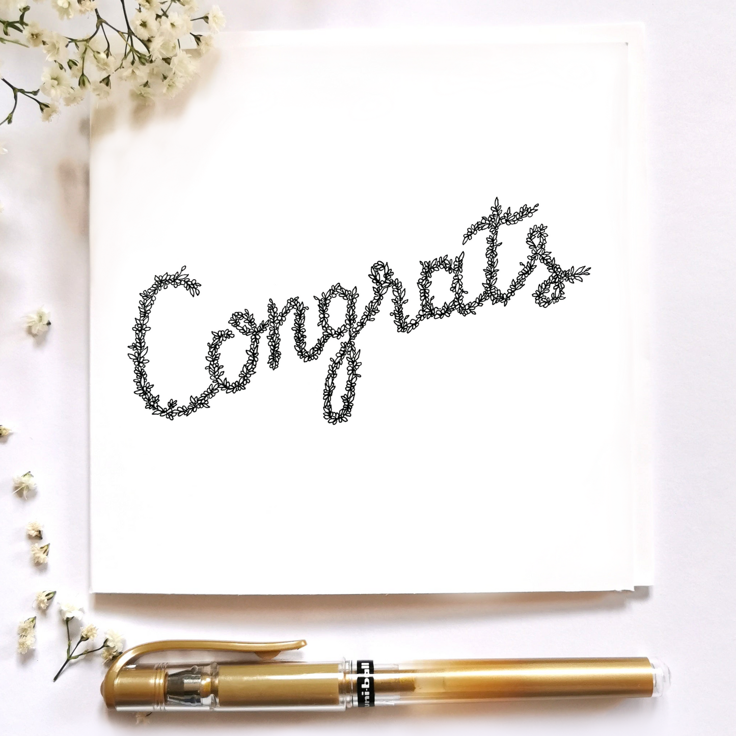 Image shows Illustration of the word Congrats drawn from floral drawings made entirely in black and white. at the bottom of the image is a gold pen and white floral arrangements to the left hand side of the image.