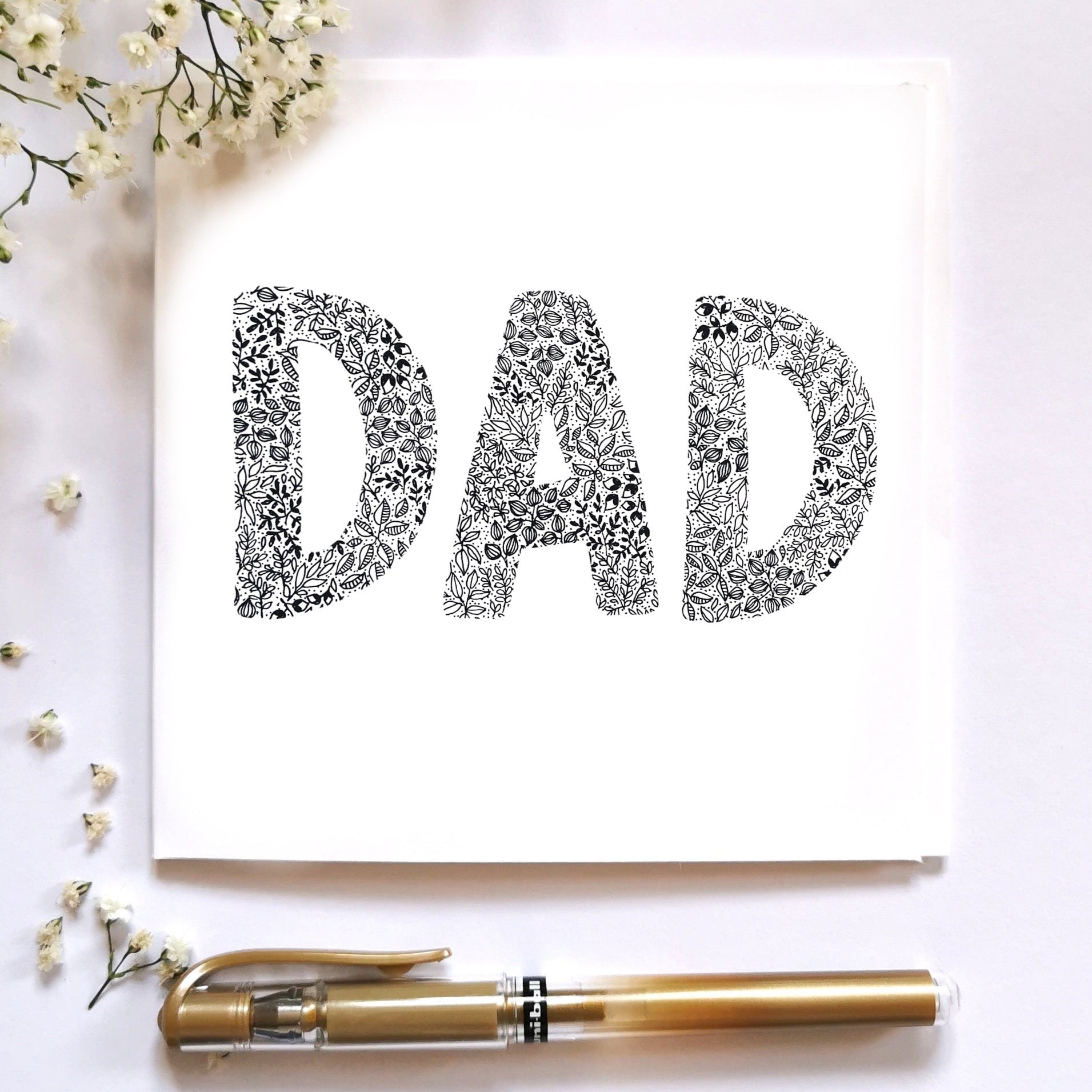 Image shows the word DAD drawn from entirely black and white floral drawings. the word DAD is centred in the middle of the illustration with a gold pen laid at the bottom of the image to show what it would look like dressed up. 