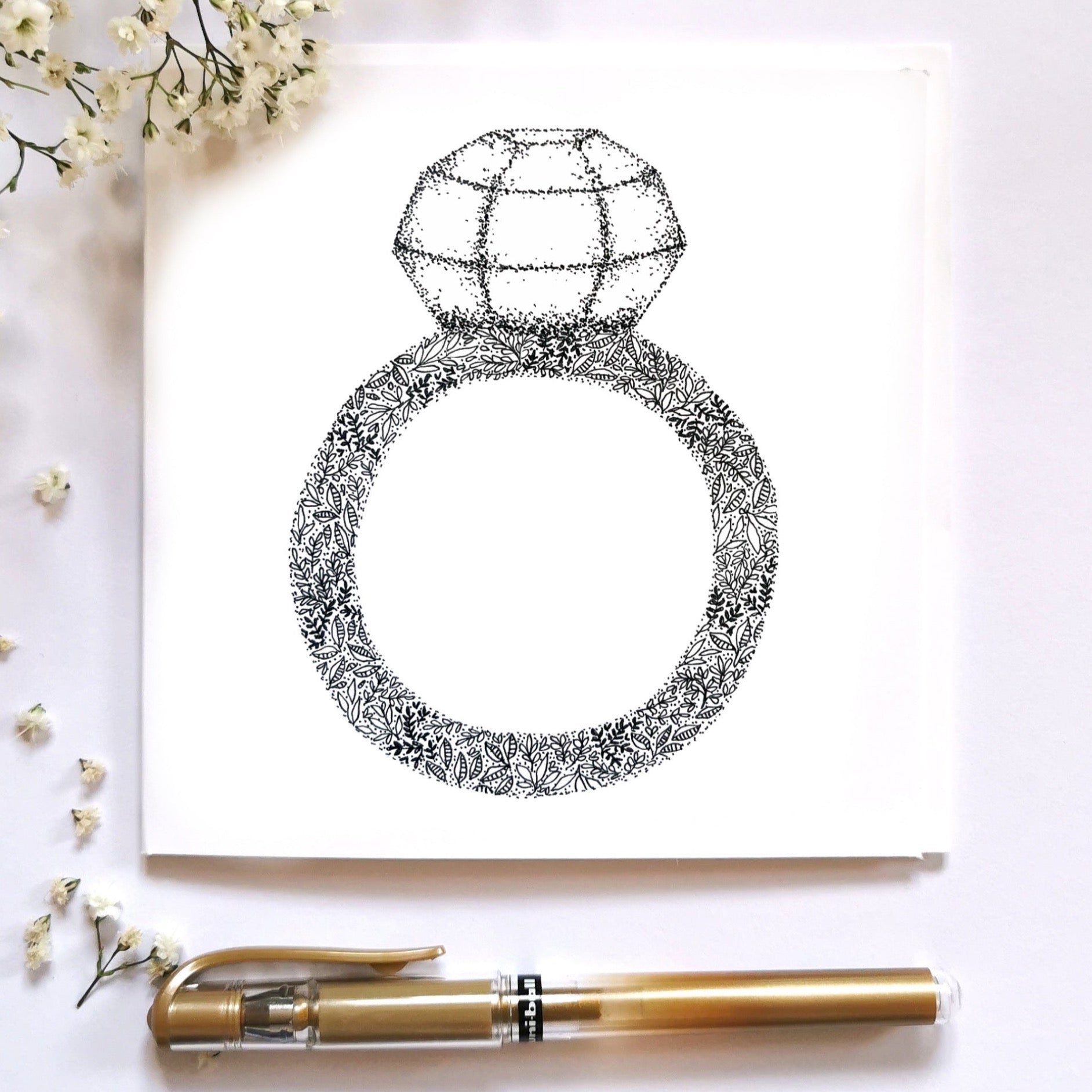 Image shows drawing of a Diamond ring drawn from flowers and black and white dots. the diamond is made entirely from different sized dots. image is laid on a cream surface with arrangements surrounding it to show the image dressed up. 