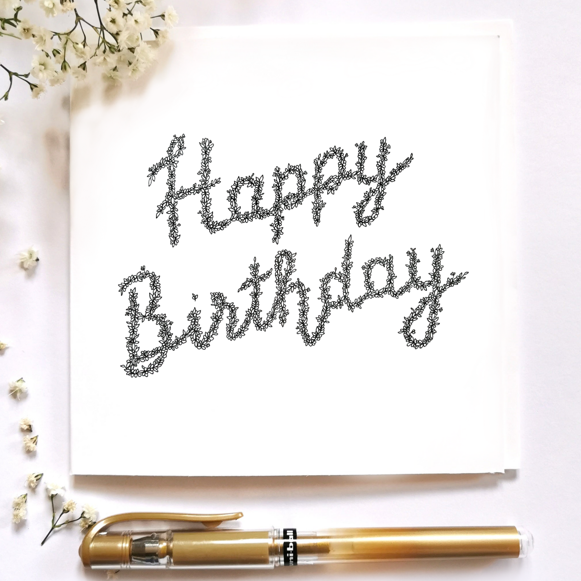 Image shows illustration Card of The phrase Happy Birthday. Happy is drawn on top whilst Birthday is drawn directly below centred of the page. Illustration is surrounded by a gold pen and white flowers. 