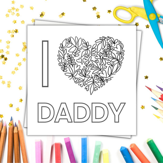 Image shows colour in card with the phrase I LOVE YOU DADDY . LOVE is a heart made from floral drawings and tiny hearts. Image laid on a white surface with colourful crayons pencils and gold stars.
