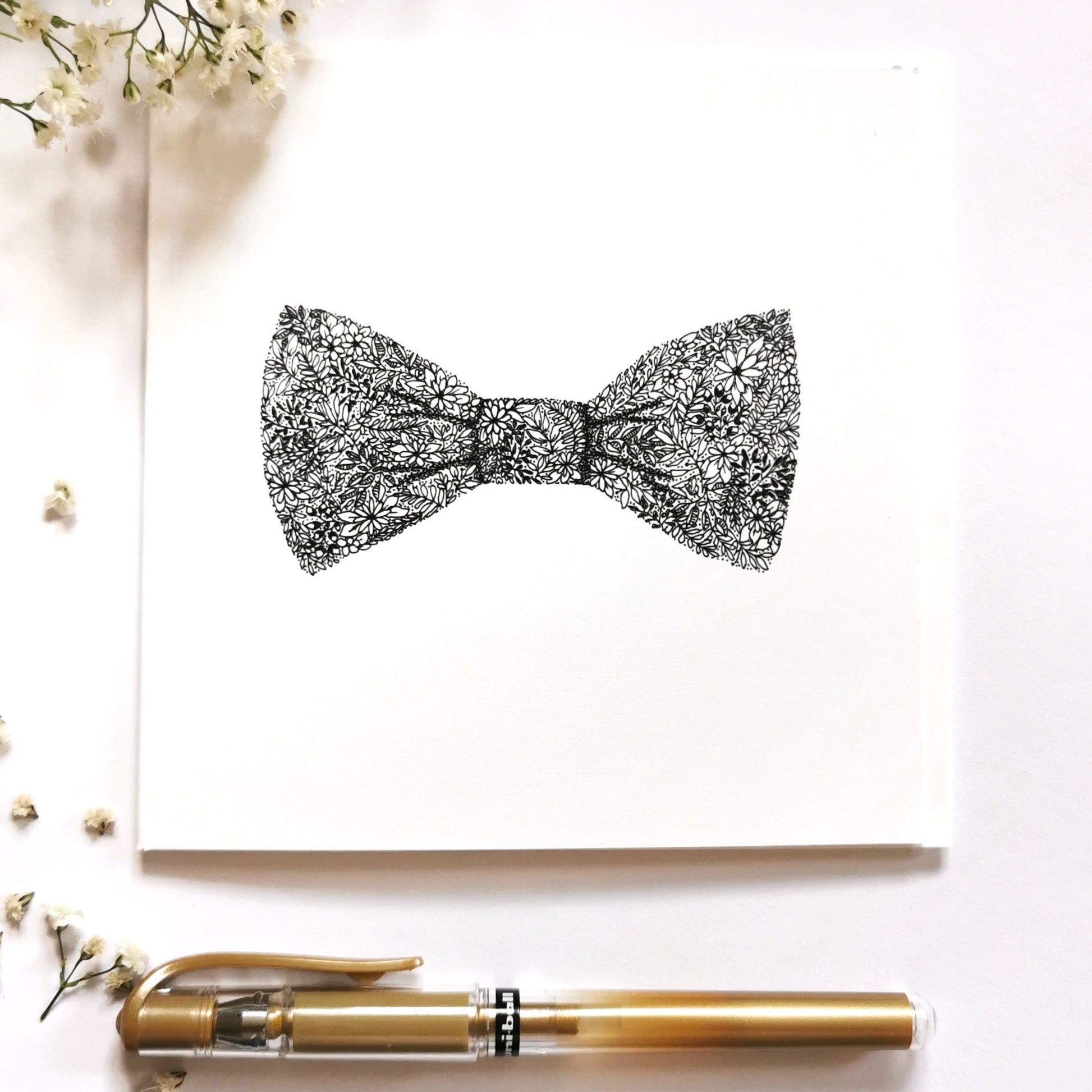 Illustrations shows black and white bow drawing made up from variety of flowers and plants. Bow is placed centre middle of image with a gold pen at the bottom of the picture and a few white blossom flowers on the bottom and top left corner to show what image would look dressed up.