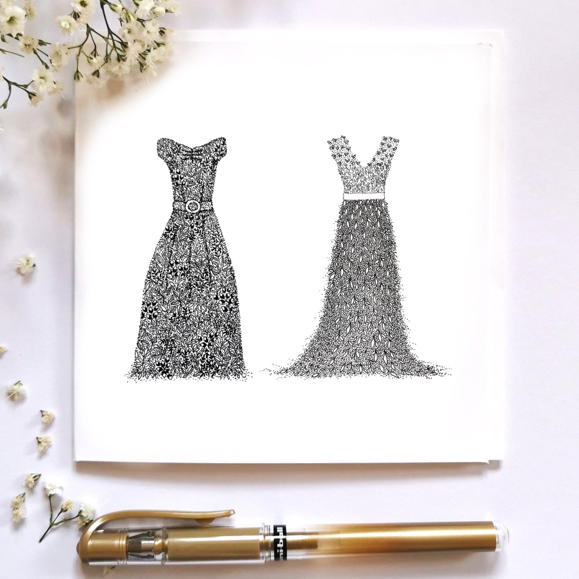 Image shows MRS & MRS card illustration. both titles are portrayed by dresses, the one on the left being a short sleeve dress with belt in the middle and more structure and the one to the right being a floral summer-y vibe dress more flowy. Both dresses are hand drawn using floral drawings. Image entirely black and white. Image is displayed on a cream surface with floral arrangements and a gold pen surrounding it to show image dressed up. 